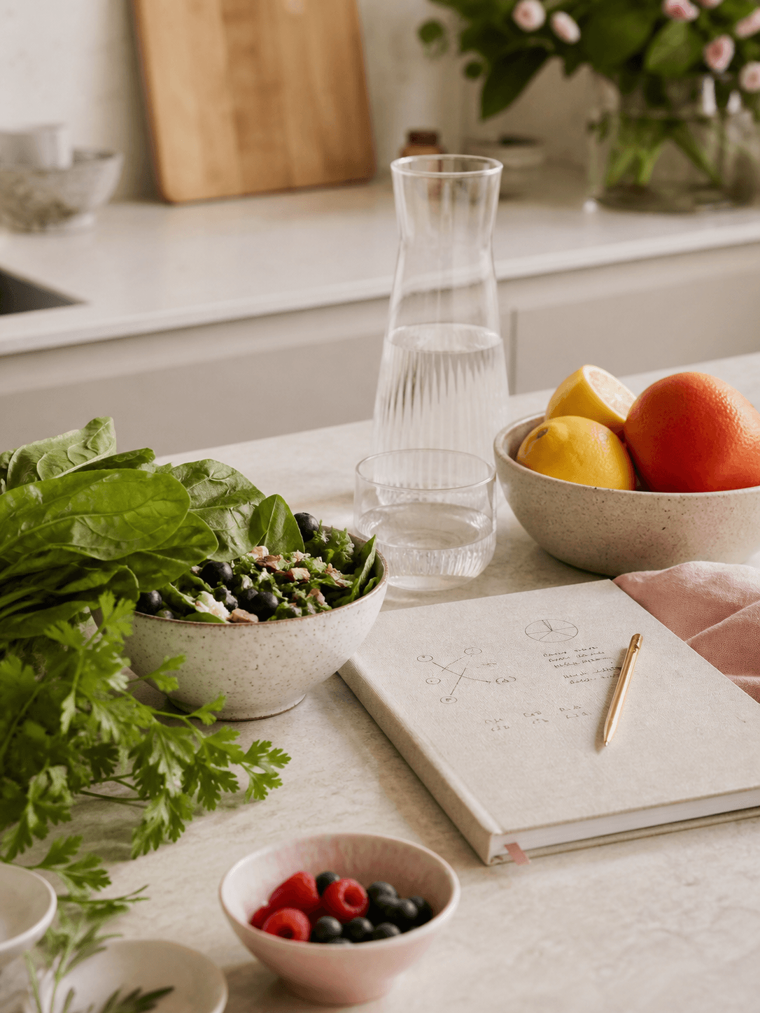 Fresh salad, fruit, water, and an open nutrition-planning notebook on a kitchen counter